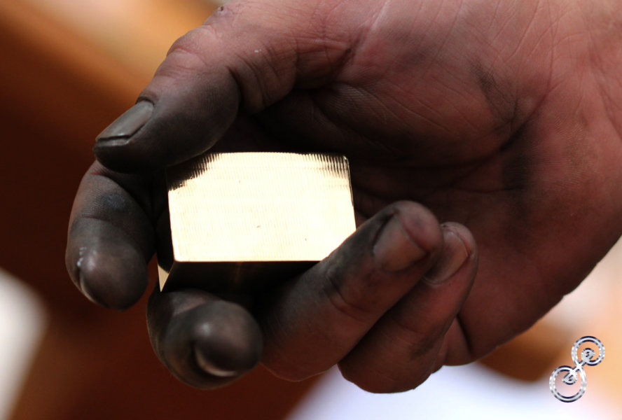 Hand black from polishing holding a gold bar of brass